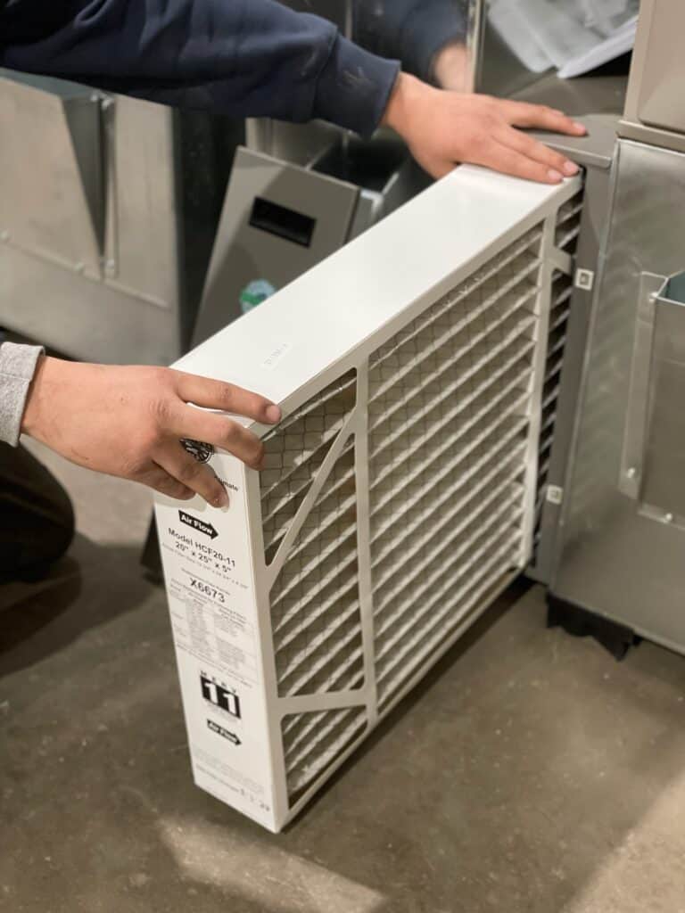 Technician sliding a thick MERV 11 media filter sideways into a furnace filter cabinet