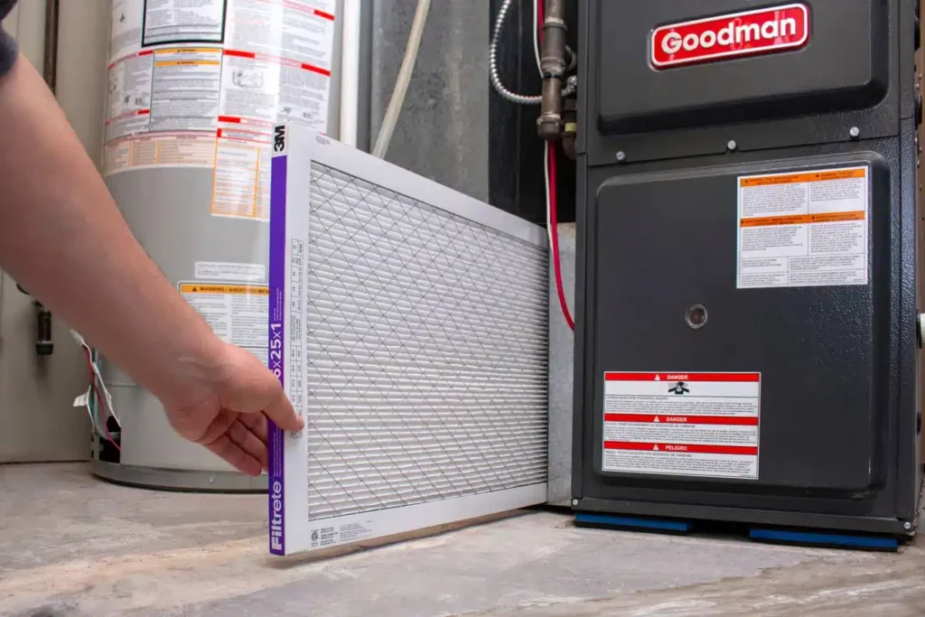 Hand sliding a new pleated air filter sideways into the filter slot of a Goodman furnace